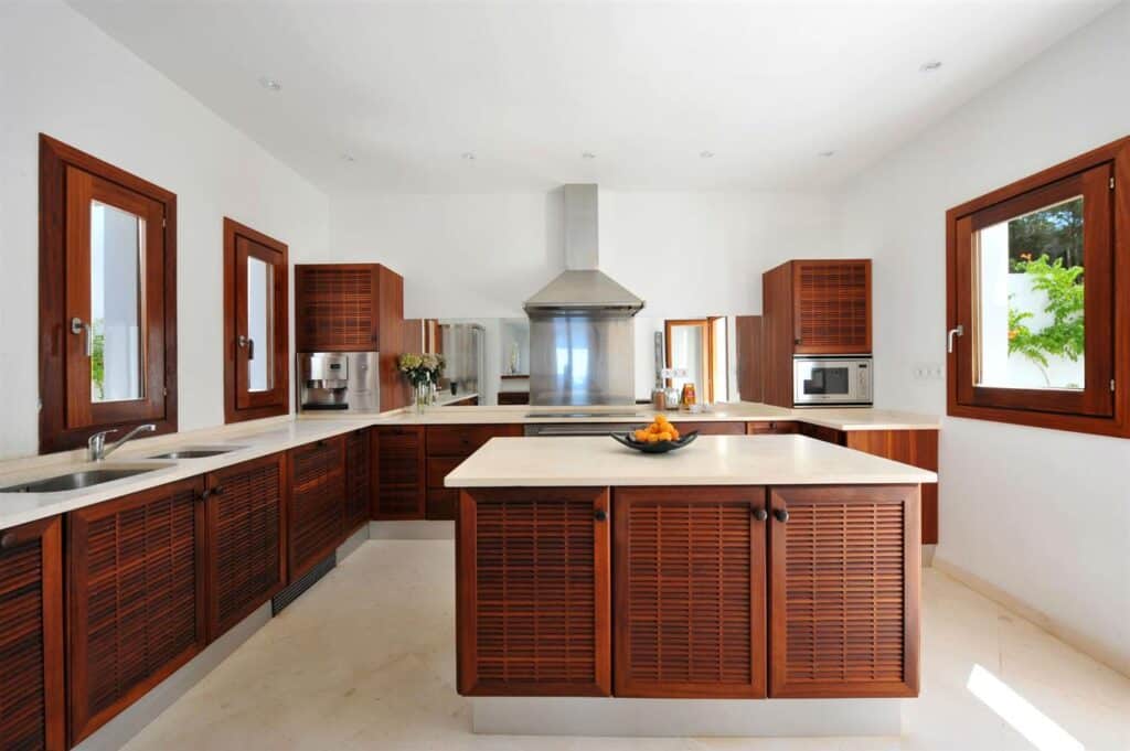 Modern kitchen reminiscent of luxury travel, featuring a central island with light countertops and dark wood cabinetry. Stainless steel appliances are seamlessly integrated into the design. Large windows provide ample natural light, and a bowl of fruit is elegantly placed on the island. David Pearson Travel