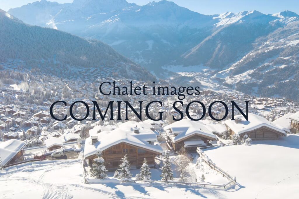A snowy mountain village with wooden chalets, surrounded by pine trees and mountains under a clear blue sky. Text overlay reads: Chalet images COMING SOON. David Pearson Travel