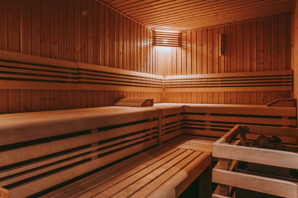Wood-paneled sauna room with wooden benches on two levels along the walls and a heater in the corner. The space is warmly lit, creating a cozy atmosphere. No people are present. David Pearson Travel
