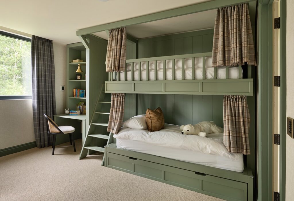 A cozy bedroom with green built-in bunk beds, plaid curtains, a white pillow and stuffed polar bear on the lower bed, a window with curtains, and a small desk with a chair and bookshelf in the corner. David Pearson Travel
