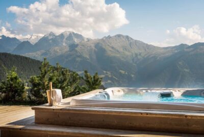 calima-ve-21 A luxurious outdoor hot tub with bubbling water overlooks a scenic mountain landscape under a partly cloudy sky. A champagne bottle in an ice bucket and a towel sit on the wooden deck nearby. David Pearson Travel