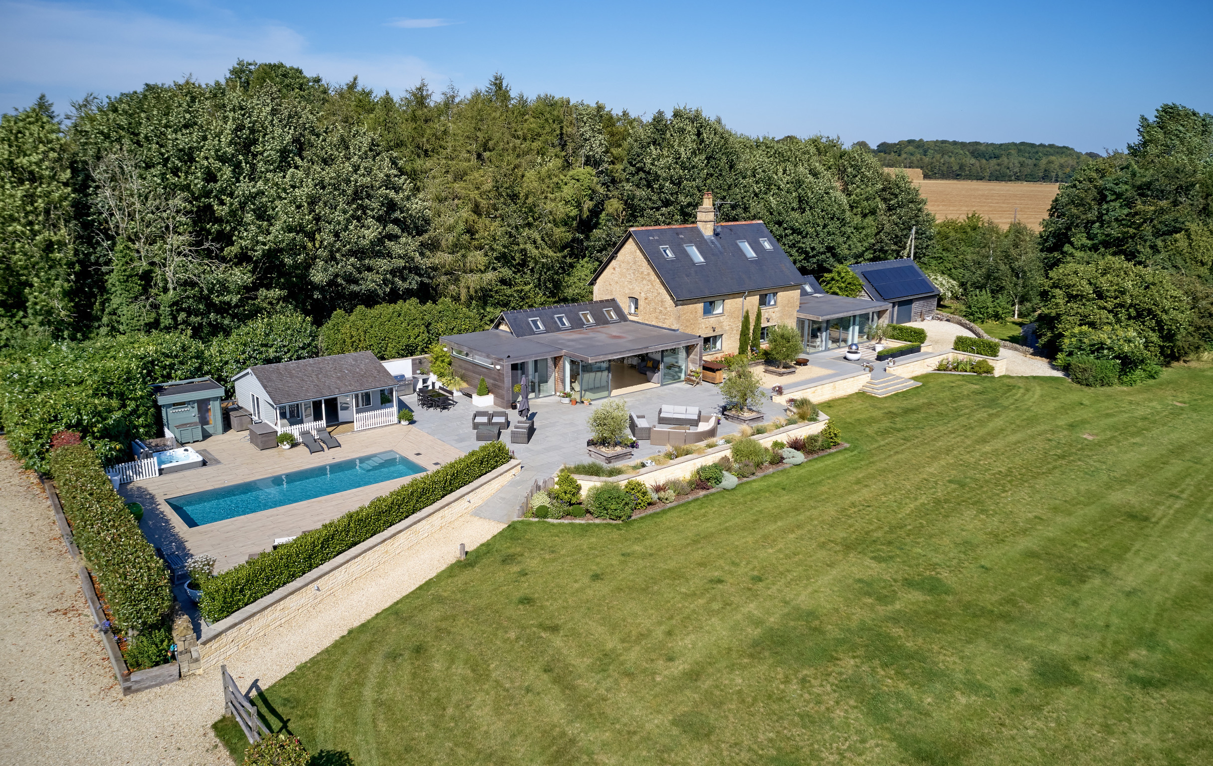 Aerial view of a large countryside house with a stone exterior, surrounded by trees and fields. The property features a swimming pool, patio seating areas, outbuildings, landscaped gardens, and an expansive lawn. David Pearson Travel