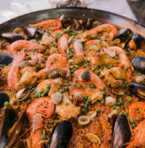A large pan of seafood paella with mussels, shrimp, clams, peas, and rice, set on a table with plates and utensils in the background—perfect for savoring during your Ibiza travel experience. David Pearson Travel