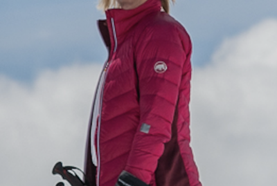 Screenshot 2026-04-08 at 13.48.46 A person wearing a bright pink jacket, green pants, and sunglasses stands outdoors in a snowy, mountainous area, holding ski poles and smiling. David Pearson Travel