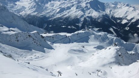 photo-1662536209013-844e0a8eced8 A scenic view of snow-covered mountains and ski slopes in Verbier, with ski lifts and trails winding through the landscape under a clear blue sky. David Pearson Travel