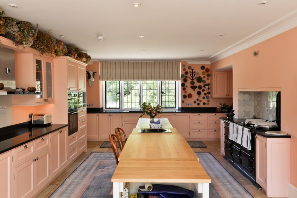 Spacious kitchen with peach cupboards, black worktops, a long wooden island, two chairs, a black range cooker, wall decorations, and large windows letting in natural light. David Pearson Travel
