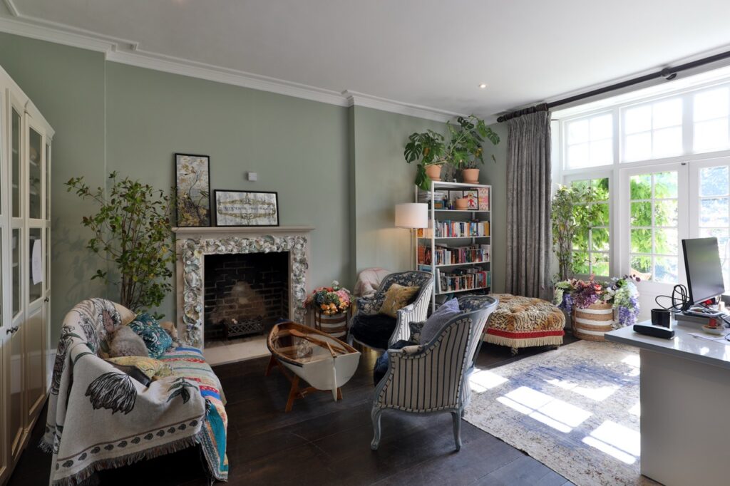 Bright living room with large windows, a fireplace, cosy seating, bookshelves, green plants, and decorative items. Sunlight streams in, creating a warm and inviting atmosphere with a mix of classic and modern décor. David Pearson Travel